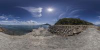 a camera lens view of the beach and sky with a sun in the background and some rocks at the edge