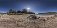 a panoramic view of the sun over sand and trees on the shore of a lake