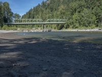 an old metal bridge over water in the forest next to a road and a mountain