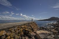 a person is on a ledge on a beach by the ocean and rocks on the shore