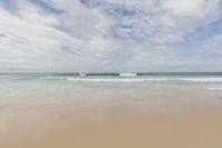 a man standing in shallow water looking at an ocean wave during the day, on the beach