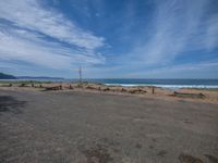 two empty benches sit in the middle of the deserted park near the ocean with a cloudy blue sky above them