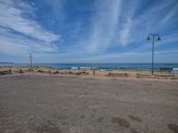 two empty benches sit in the middle of the deserted park near the ocean with a cloudy blue sky above them