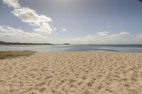 an empty beach on a clear day with some clouds in the distance and a sunny blue sky