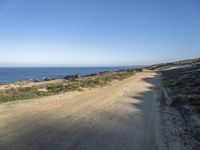 a beach with rocks and grass alongside a beach, and dirt road along the shoreline