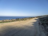 a beach with rocks and grass alongside a beach, and dirt road along the shoreline