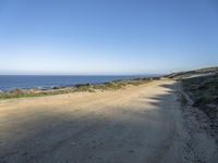 a beach with rocks and grass alongside a beach, and dirt road along the shoreline