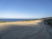 a beach with rocks and grass alongside a beach, and dirt road along the shoreline