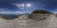 a camera lens view of the beach and sky with a sun in the background and some rocks at the edge