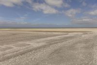 the dry, flat area in front of a vast sky with small clouds and a white car