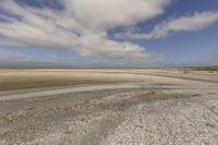 the dry, flat area in front of a vast sky with small clouds and a white car