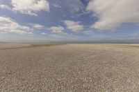 the dry, flat area in front of a vast sky with small clouds and a white car