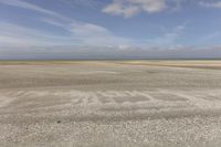 the dry, flat area in front of a vast sky with small clouds and a white car