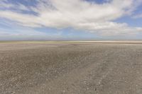 the dry, flat area in front of a vast sky with small clouds and a white car