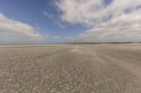 the dry, flat area in front of a vast sky with small clouds and a white car