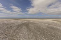 the dry, flat area in front of a vast sky with small clouds and a white car