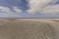 the dry, flat area in front of a vast sky with small clouds and a white car