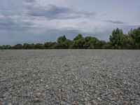 a beach and trees against a cloudy sky with some blue sky behind it, with a field of rocks