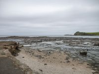 a wet sidewalk leading to the ocean with a bench in the foreground and an island in the background