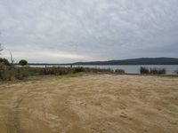 the sand area in front of a lake near a bench and bike rack with a few other picnic benches