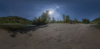 a fish eye shot of an empty beach and forest area with a bridge on the shoreline