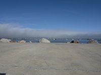 the sun is shining on some rocks along the water's edge with a dog laying at the edge and boats sailing in the distance