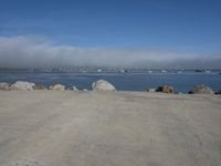 the sun is shining on some rocks along the water's edge with a dog laying at the edge and boats sailing in the distance