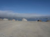 the sun is shining on some rocks along the water's edge with a dog laying at the edge and boats sailing in the distance