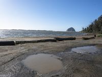 water puddles on the sand and a rocky coast in the distance, there's another body of water next to it