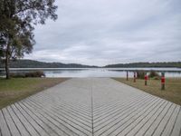 a large wooden walkway next to a body of water with trees in the background and a dock that has several post holding red stop lights on each end posts