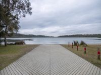 a large wooden walkway next to a body of water with trees in the background and a dock that has several post holding red stop lights on each end posts