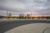 a paved walkway is by the river at dusk with an orange hue in the sky