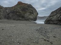 there are three big rocks in the sand with waves coming in through them, on a beach next to the ocean