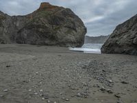 there are three big rocks in the sand with waves coming in through them, on a beach next to the ocean