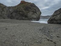 there are three big rocks in the sand with waves coming in through them, on a beach next to the ocean