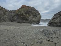 there are three big rocks in the sand with waves coming in through them, on a beach next to the ocean