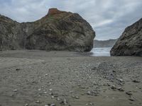 there are three big rocks in the sand with waves coming in through them, on a beach next to the ocean