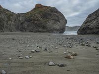 there are three big rocks in the sand with waves coming in through them, on a beach next to the ocean