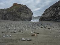 there are three big rocks in the sand with waves coming in through them, on a beach next to the ocean