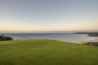 the sun is setting over a grassy golf course near an ocean and sandy beach behind it