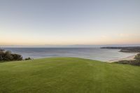 the sun is setting over a grassy golf course near an ocean and sandy beach behind it