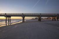 the bridge over the sand leading to the beach and ocean with buildings in the background