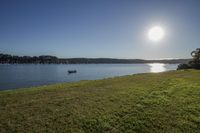 a small boat floating down a body of water near a shore line with a setting sun