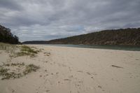 a sandy beach with a body of water in the distance and hills on both sides