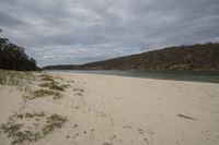 a sandy beach with a body of water in the distance and hills on both sides