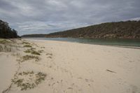 a sandy beach with a body of water in the distance and hills on both sides