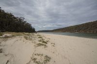 a sandy beach with a body of water in the distance and hills on both sides