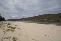 a sandy beach with a body of water in the distance and hills on both sides