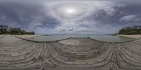 a fish eye lens picture shows the view of water, beach and a dock at a pier