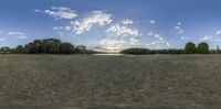 the wide open field with a large cloud in the sky at dusk near a lake